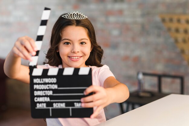 Lächelndes schönes Mädchen, das clapperboard hält