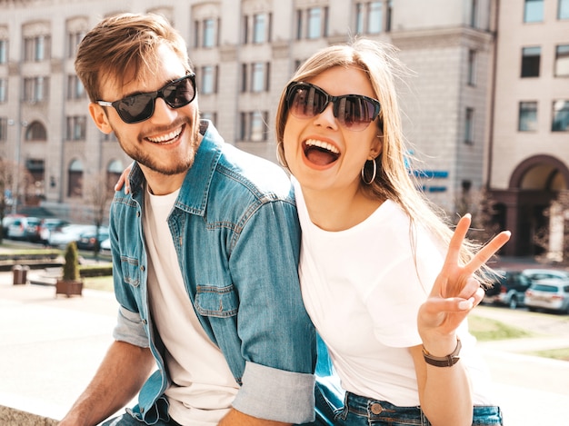 Lächelndes schönes Mädchen und ihr hübscher Freund in der zufälligen Sommerkleidung. . Zeige Friedenszeichen