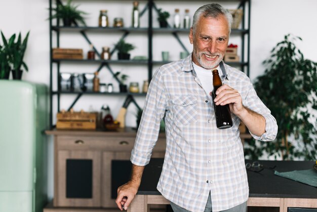 Lächelndes trinkendes Bier des älteren Mannes von der Flasche zu Hause