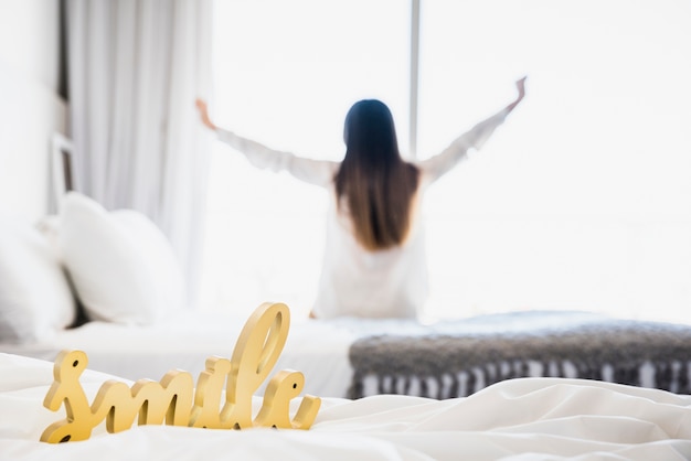 Lächelnwort auf weißer Decke mit der Frau, die ihre Hände am Hintergrund ausdehnt