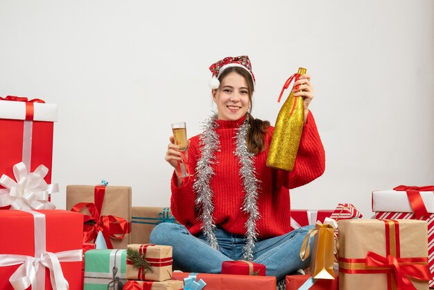 lächelte Mädchen mit Weihnachtsmütze, die Champagner und Glas hält, die Geschenke auf Weiß sitzen