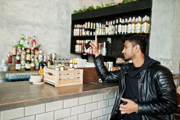 Kostenloses Foto lässige und stilvolle junge asiatische mann tragen auf lederjacke sitzen auf bar und halten kreditkarte für die bezahlung