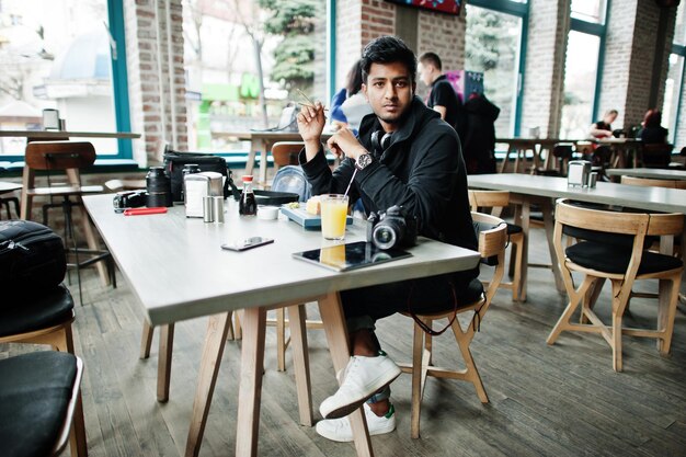 Lässiger und stilvoller junger asiatischer Mann mit Kopfhörern im Café, das Sushi isst