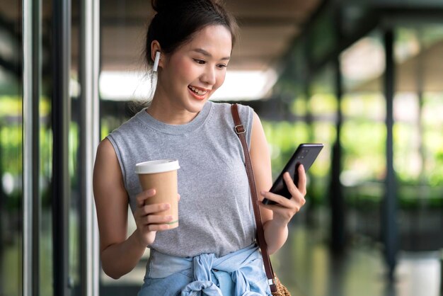 Lässiges Gehen während der Geschäftsdiskussion im Bürokorridorasiatische weibliche digitale Nomaden-freiberufliche Unternehmerin beiläufiges Arbeiten während der Reise Urlaub im Korridor im Freienlächelndes weibliches Smartphone