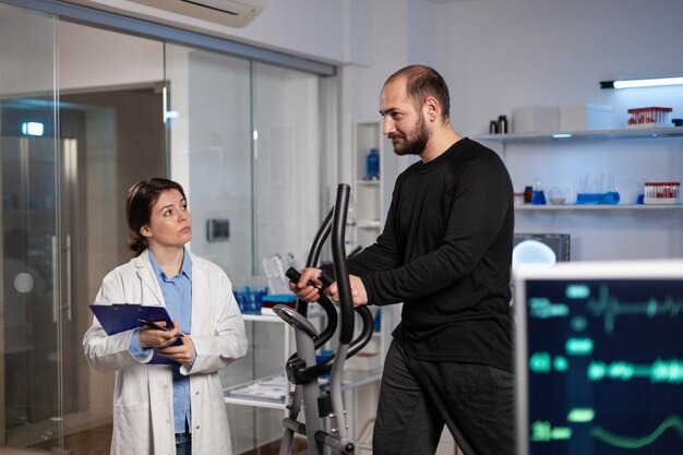 Läufer in Sportgeräten, die während der medizinischen Untersuchung im modernen Labor an der Körperausdauer arbeiten, während die Forscherin EKG-Daten zur Messung des Herzfrequenzpulses analysiert. Medizinservice