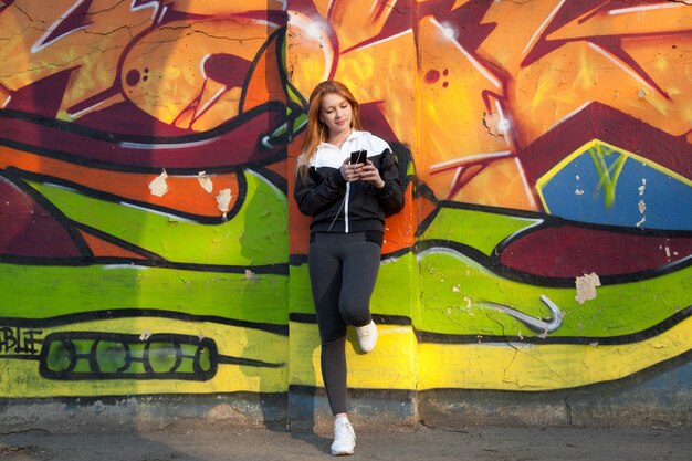 Läufer Mädchen ruht mit Handy gegen helle Graffiti-Wand