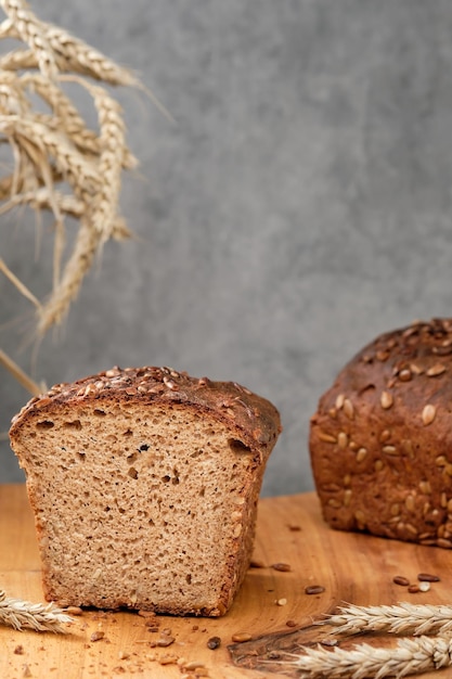 Laib Weizen-Roggen-Sauerteigbrot mit Sonnenblumenkernen auf einem Schneidebrett. Frisch gebackene dunkle Brothälften, Nahaufnahme selektiver Fokus. Weizenähren auf dem Tisch