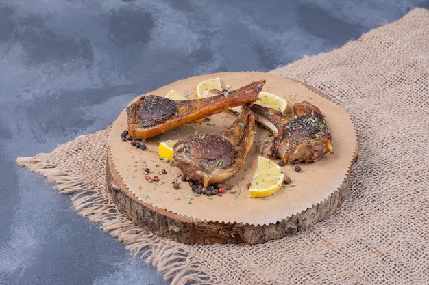 Lammfleisch auf Holzbrett mit Zitronenscheiben und Besteck auf Tischdecke.