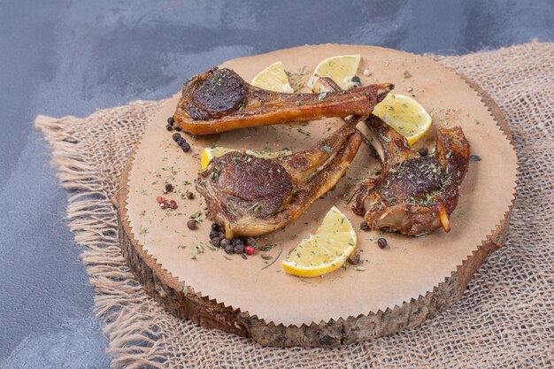 Lammfleisch auf Holzbrett mit Zitronenscheiben und Besteck auf Tischdecke.