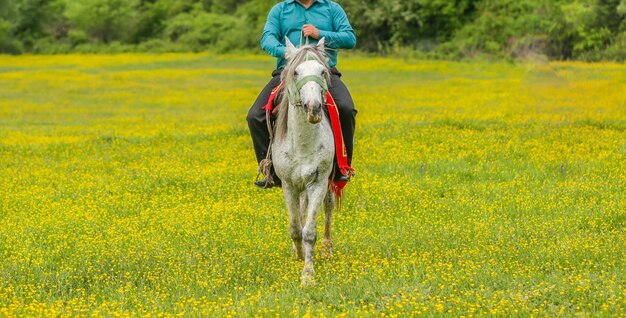 Landarbeiter, der in einer Bauernhofzone mit grünem Gras und gelben Blumen reitet