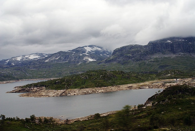 Landschaft einer Landschaft mit einem See, umgeben von grünen Bergen unter einem bewölkten Himmel in Norwegen