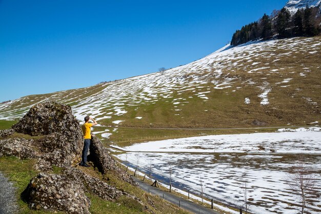 Landschaft eines jungen Mannes, der zwischen den Felsen in den Bergen mit etwas Schnee steht