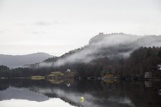 Landschaft eines Sees umgeben von Bergen bedeckt mit Wäldern und Nebel, der auf dem Wasser reflektiert