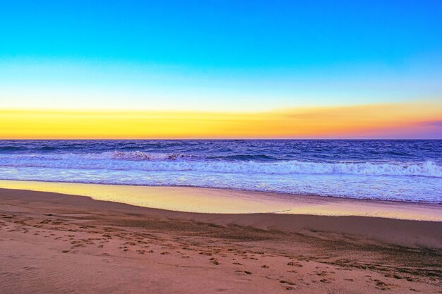 Landschaft eines Strandes, umgeben von Meereswellen während eines orangefarbenen Sonnenuntergangs am Abend