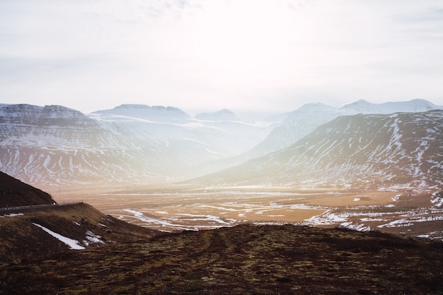 Landschaft von Hügeln bedeckt im Gras und im Schnee unter einem bewölkten Himmel und Sonnenlicht in Island