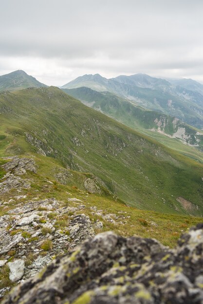 Landschaft von Hügeln bedeckt im Grünen mit felsigen Bergen unter einem bewölkten Himmel