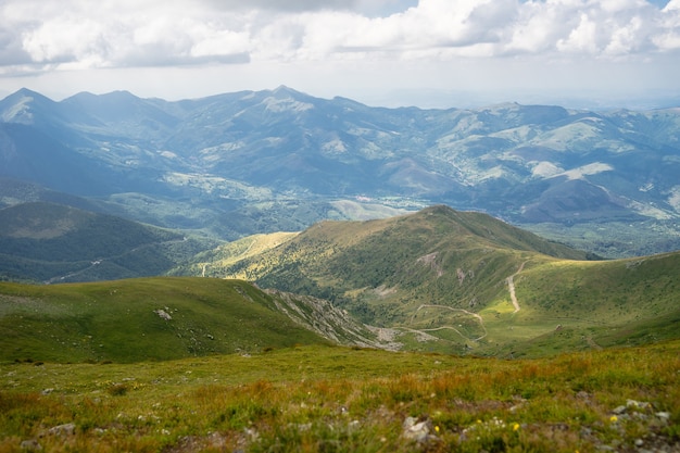 Landschaft von Hügeln bedeckt mit Gras und Bäumen unter einem bewölkten Himmel und Sonnenlicht während des Tages