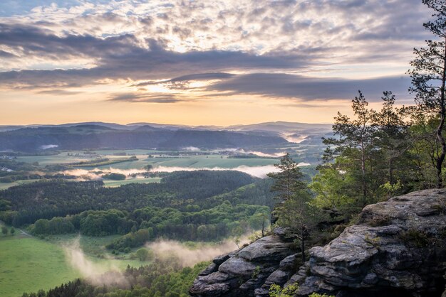 Landschaft von Hügeln, die während des Sonnenuntergangs auf dem Land mit Grün und Nebel bedeckt sind