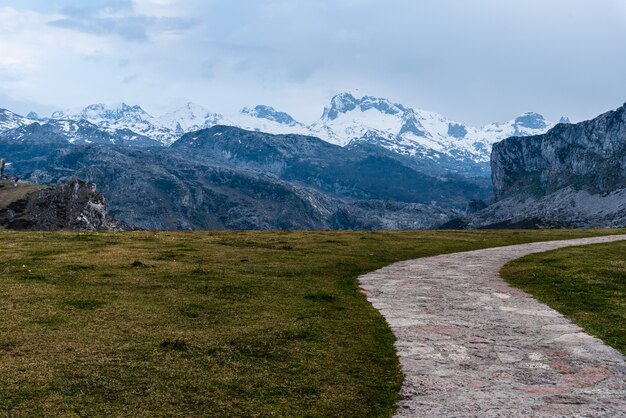 Landschaftsansicht der mit Schnee bedeckten felsigen Berge mit Gras und einer Straße im Vordergrund