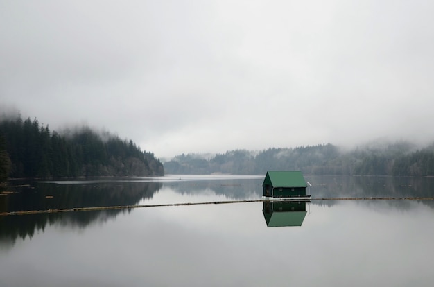 Landschaftsaufnahme eines Sees mit einem kleinen grünen schwimmenden Haus in der Mitte während eines nebligen Wetters