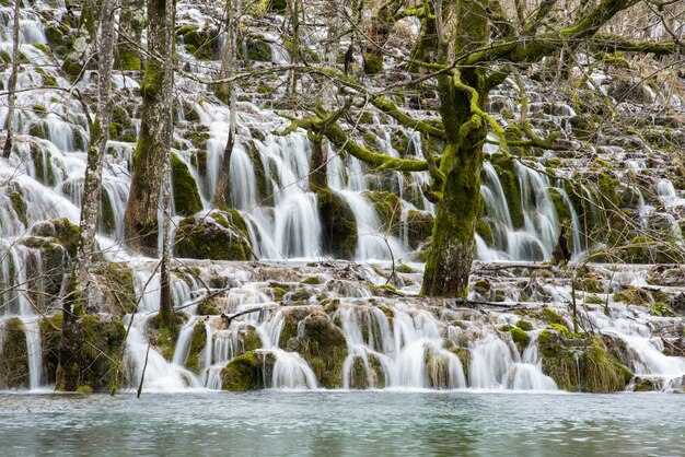 Kostenloses Foto landschaftsaufnahme eines wasserfalls, der von moosigen klippen in einen see fließt