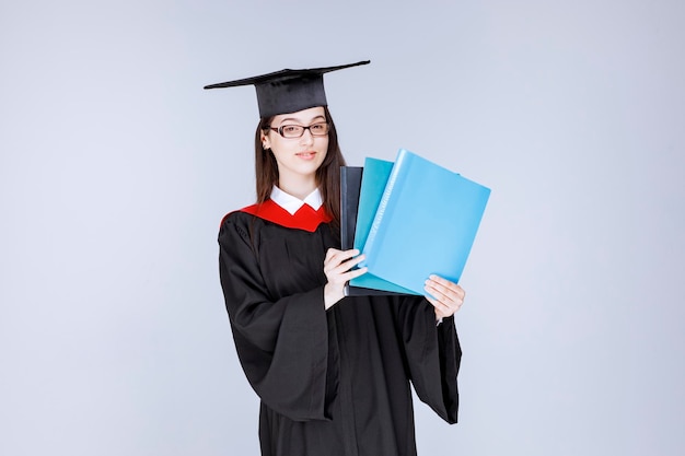 Langhaariger Student in Brille mit blauen Ordnern. Foto in hoher Qualität