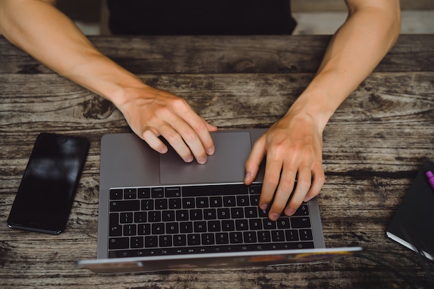 Laptop auf einem Holztisch, Hände eines Mannes, der an einem Computer arbeitet