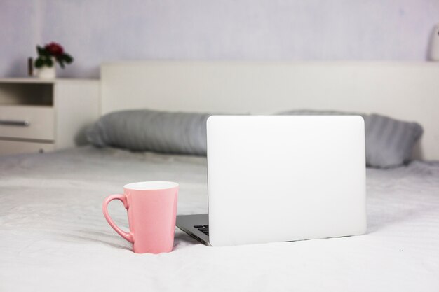 Laptop auf weißem Bett mit Kaffeetasse