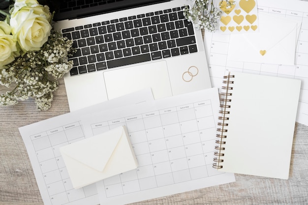 Kostenloses Foto laptop; blumen; briefumschlag; kalender und spiralblock auf schreibtisch aus holz