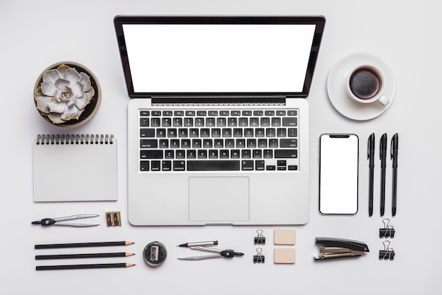 Kostenloses Foto laptop; handy; tasse kaffee und büromaterial auf weißem hintergrund
