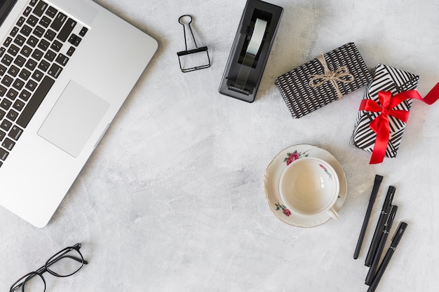 Laptop in der Nähe von Präsentkartons, Tasse auf Teller und Briefpapier