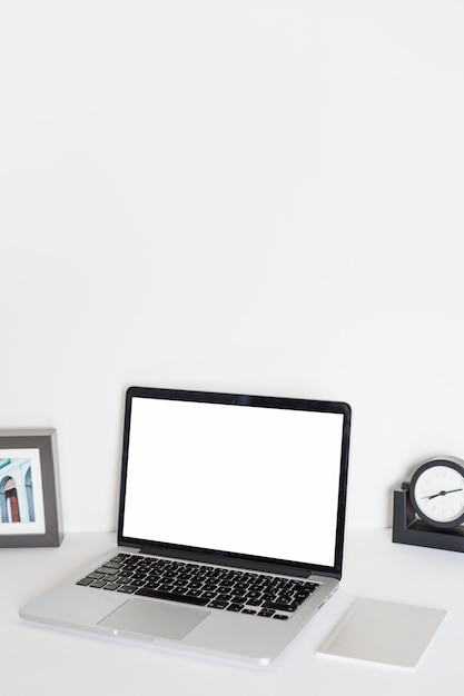 Laptop in der Nähe von Tischuhr, Fotorahmen und Papier