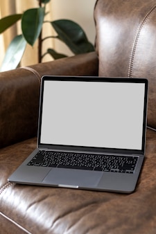Laptop mit leerem bildschirm auf einer ledercouch