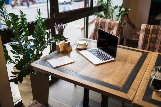 Laptop mit Notizblock im Café auf Tabelle