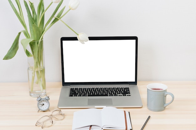 Laptop mit weißen Tulpen im Vase auf Holztisch