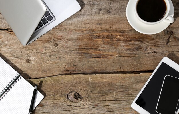 Laptop, Notizblock und Stift auf dem Tisch mit einer Tasse Kaffee und mit anderen Geräten