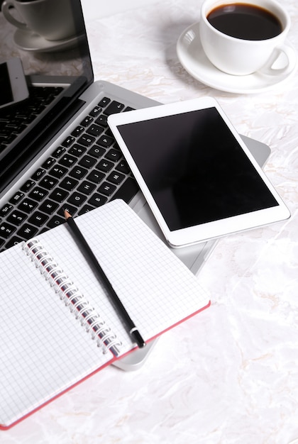 Laptop, Notizblock und Stift auf dem Tisch mit einer Tasse Kaffee und mit anderen Geräten