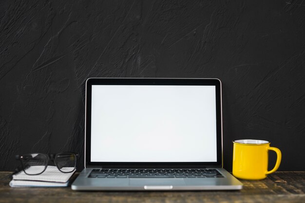 Laptop; Schauspiel; gelbe Kaffeetasse und Tagebuch auf Tabelle mit schwarzer strukturierter Wand