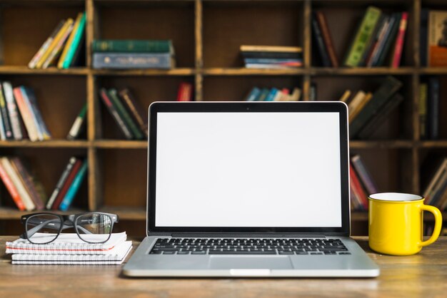 Laptop; Tasse; Brille und Spiralblock auf Schreibtisch aus Holz