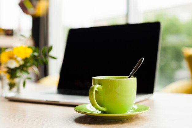 Laptop und grüne keramische Kaffeetasse auf Arbeitsschreibtisch