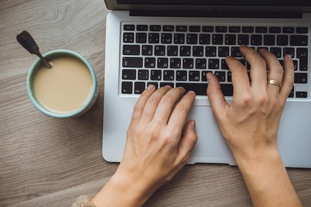 Laptop und Kaffeetasse in den Händen des Mädchens, die auf einem hölzernen Hintergrund sitzen