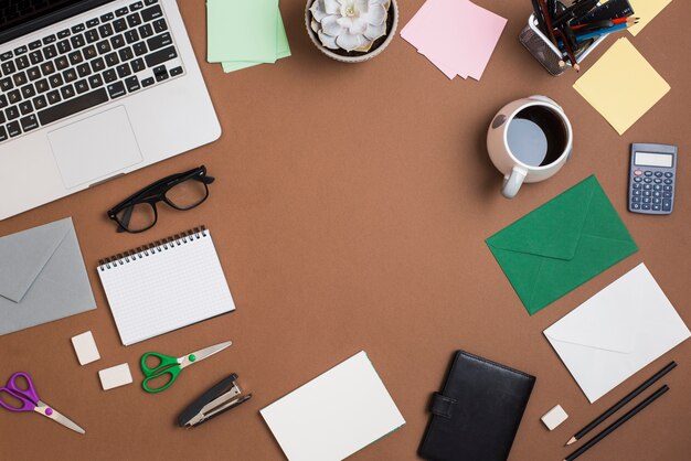 Laptop und Kaffeetasse mit Briefpapier auf braunem Desktop