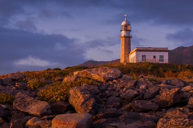 Larino Leuchtturm umgeben von Felsen während des Sonnenuntergangs in Spanien