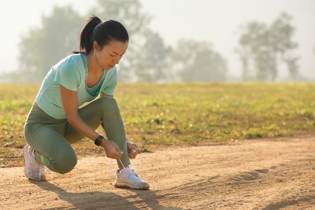 Laufschuhläuferfrau, die Schnürsenkel für den Herbstlauf im Waldpark bindet. Läufer, die Laufschuhe ausprobieren, bereiten sich auf den Lauf vor. Joggen Mädchen Übung Motivation Gesundheit und Fitness.