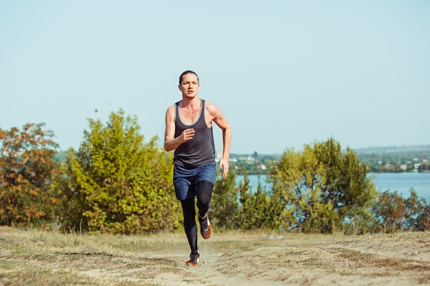 Laufsport. mannläufer, der im freien in der landschaftlich reizvollen natur sprintet. fit muskulöses männliches athleten-trainings-trailrunning für den marathonlauf. sportlich fit sportlicher mann, der im sprint in kompressionskleidung trainiert