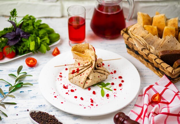 Lavashsnackrolle mit Käse- und Granatensamen, Brot, Gemüse und Sorbet auf einer weißen Platte. Snack