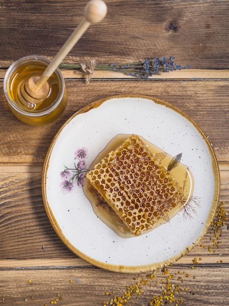 Kostenloses Foto lavendel; honigtopf mit hölzernen honigschöpflöffel und bienenpollen auf holztisch