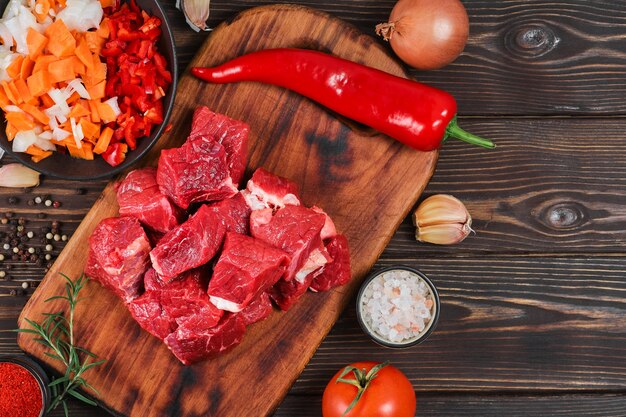 Layout der Zutaten zum Kochen von Gulasch oder Eintopf. rohes Rindfleisch, Gemüse, Gewürze, auf rustikalem Holztisch