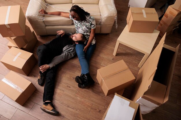 Lebenspartner träumen von einer zukünftigen Familie in einer neuen Mietwohnung und entspannen sich nach dem Einzug auf dem Wohnzimmerboden. Glücklich und stolz auf den Umzug des Haushalts, die Lebensleistung. Draufsicht auf.