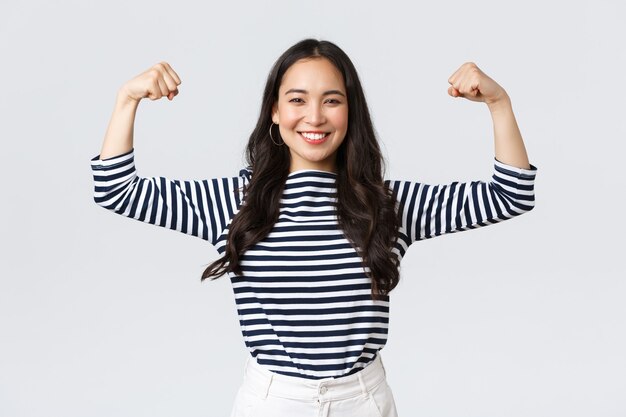 Lebensstil, Emotionen der Menschen und lässiges Konzept. Starke und selbstbewusste Asiatin beugen Bizeps, prahlen mit ihrer perfekten Form nach der Anmeldung im Fitnessstudio, prahlen mit Muskeln, trainieren und fühlen sich stark